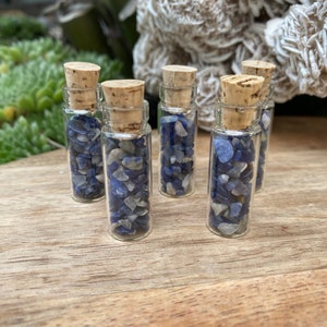 Puede incluir: Seis pequeñas botellas de vidrio con tapas de corcho llenas de piedras preciosas azules y blancas.