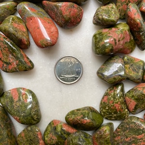 Puede incluir: Una colección de piedras pulidas verdes y rojas, también conocidas como aventurina, con una moneda canadiense de 10 centavos para la escala.