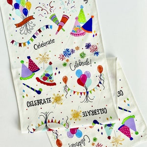 May include: White fabric table runner with a hand-painted party theme. The design includes colorful balloons, confetti, party hats, fireworks, and the words "Party" and "Celebrate". The phrase "happy day" is also included.