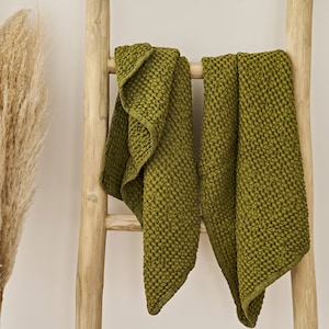 Puede incluir: Dos toallas de tejido de waffle verde oliva colgadas de una escalera de madera.