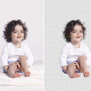 May include: A young child with curly brown hair is sitting on a white blanket. The child is wearing a white long-sleeved shirt and blue and white patterned shorts. The child is smiling and looking at the camera.
