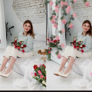May include: A woman in a light blue jacket with a white and blue pattern sits on a white bed with a bouquet of red and pink tulips in her lap. She is wearing white pants and white heels. The background is a white brick wall.