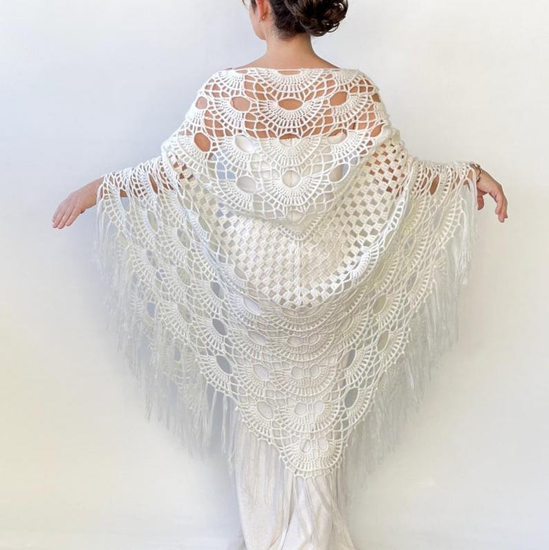 May include: White crochet shawl with a fringe border. The shawl has a delicate, lacy pattern with a circular design in the center.