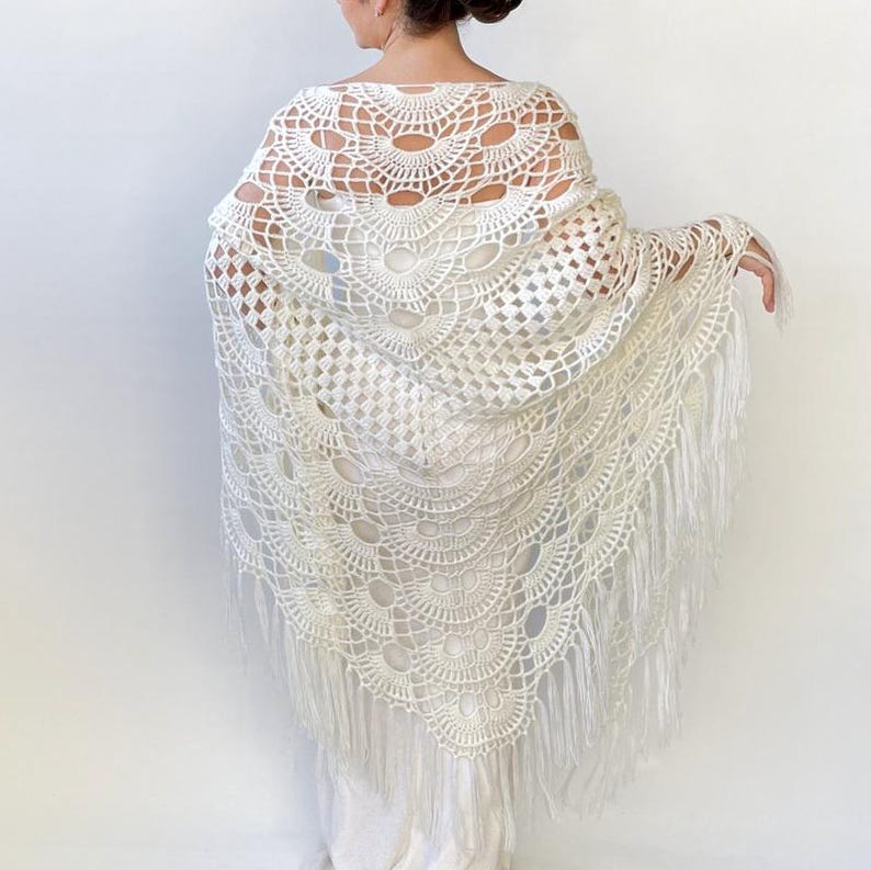 May include: White crochet shawl with a scalloped design and fringe trim. The shawl is made of delicate, openwork crochet and has a flowing, elegant look.