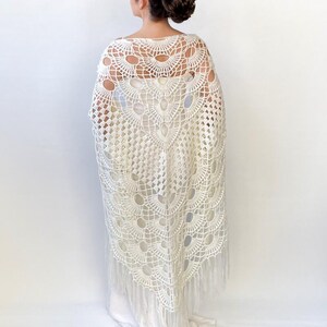 May include: White crochet shawl with a fringe border. The shawl has a delicate, lacy pattern with a scalloped edge.