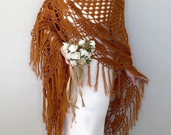 May include: A crocheted shawl with a brown color and fringe. The shawl is made with a delicate openwork pattern.