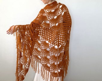 May include: A brown crocheted shawl with fringe. The shawl has a lacy pattern with large open circles.