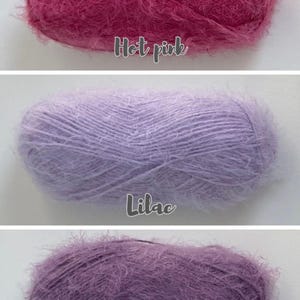 Op de afbeelding: Drie pluizige garenbollen in roze, lavendel en paarse tinten. De bovenste bol is felroze, de middelste is lila en de onderste is violet. Elke bol heeft een zachte, fuzzy textuur, perfect voor brei- of haakprojecten.