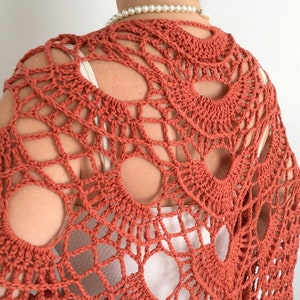 May include: A terracotta crocheted shawl with a lacy design. The shawl has a large openwork pattern with circular motifs.