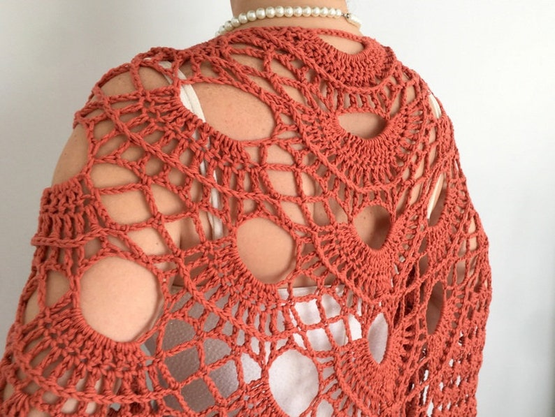 May include: A terracotta crocheted shawl with a lacy design. The shawl has a large openwork pattern with circular motifs.