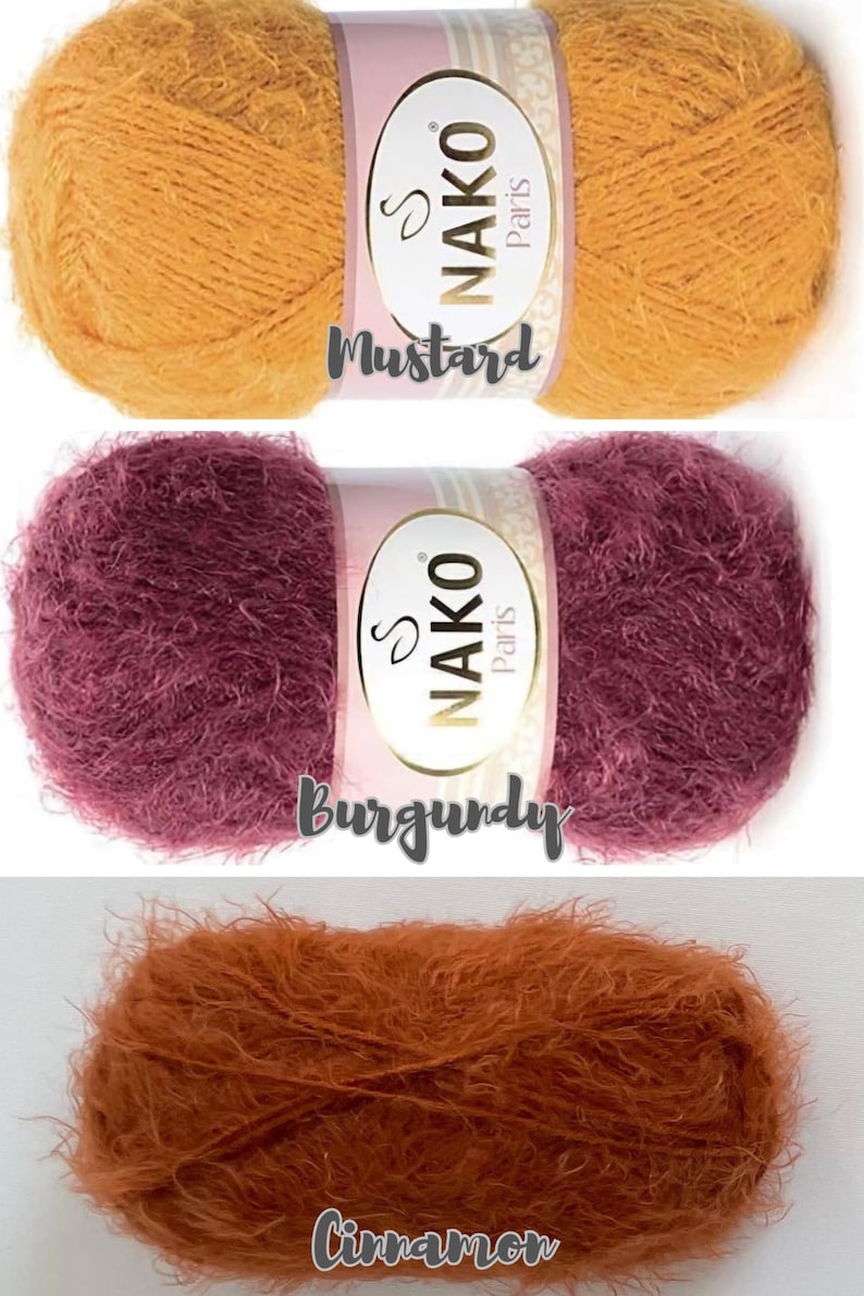 Op de afbeelding: Drie bollen Nako Paris garen in mosterd, bordeaux en kaneel kleuren. Elke bol heeft een label met de merknaam en kleurnaam. Het garen ziet er zacht en pluizig uit, geschikt voor brei- of haakprojecten.