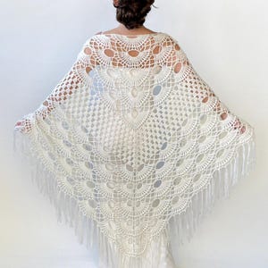 May include: White crochet shawl with a fringe border. The shawl has a delicate, lacy pattern with a circular design in the center.