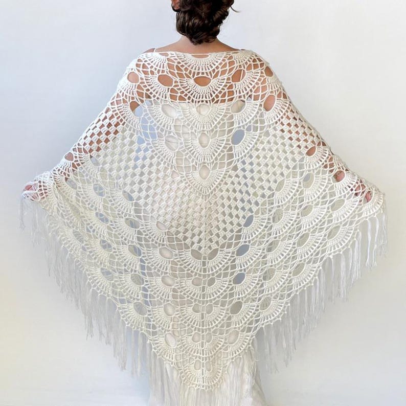 May include: White crochet shawl with a fringe border. The shawl has a delicate, lacy pattern with a circular design in the center.