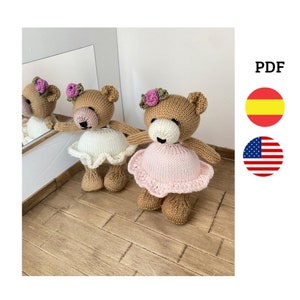 Puede incluir: Dos osos de peluche tejidos de color marrón que llevan vestidos rosas y blancos con diademas de flores. Los osos están de pie sobre un suelo de madera.