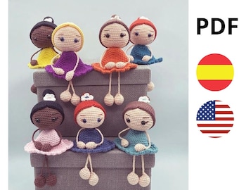 May include: Seven crocheted dolls with different colored dresses and skin tones sitting on a gray box. The dolls have long legs and are wearing flower crowns. The image includes the word "PDF" in the top right corner and flags for Spain and the United States.