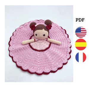 Peut inclure: Une couverture pour bébé en crochet rose avec une poupée en crochet au centre. La poupée a les cheveux bruns, une robe rose et une bordure bordeaux. La couverture a un bord festonné.