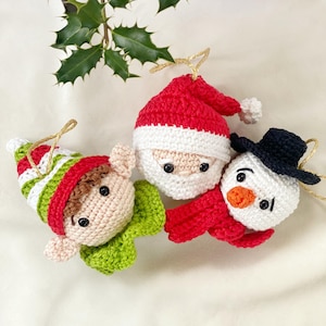 May include: Three crocheted Christmas ornaments: a red and white Santa Claus, a green and white elf, and a white snowman with a black hat and red scarf.