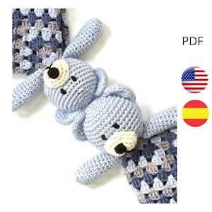 May include: Two crocheted blue teddy bears with beige faces and black eyes. The bears are attached to a blue, gray, and white crocheted blanket.