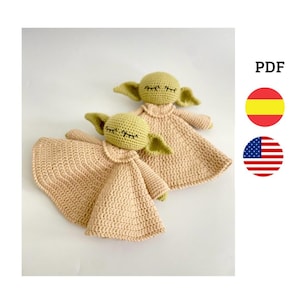 Puede incluir: Dos juguetes de peluche tejidos a crochet en forma de un personaje ficticio popular. Los juguetes son verdes con los ojos cerrados y tienen una manta de crochet beige. Los juguetes están sobre un fondo blanco.