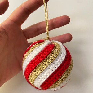May include: A red, white, and gold crocheted Christmas ornament with a gold string.