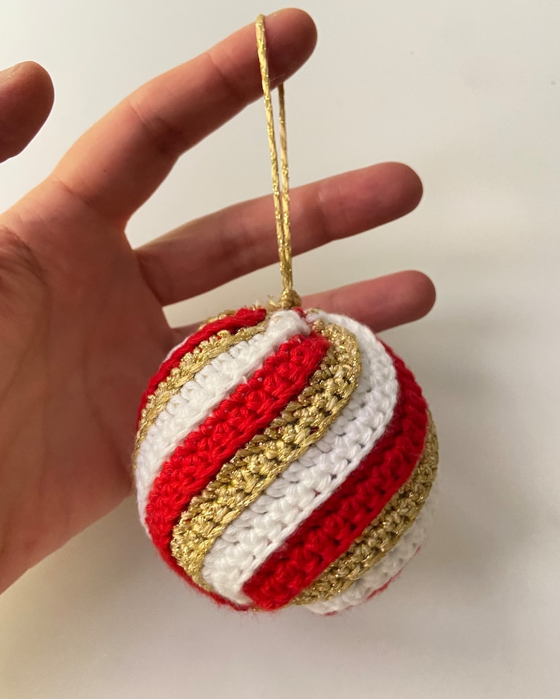 May include: A red, white, and gold crocheted Christmas ornament with a gold string.