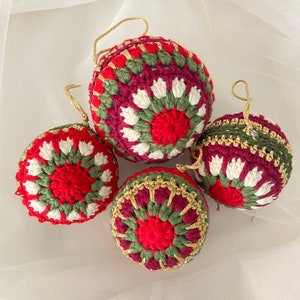 May include: Four crocheted Christmas ornaments in red, green, and white with gold accents. The ornaments are round and have a textured surface.
