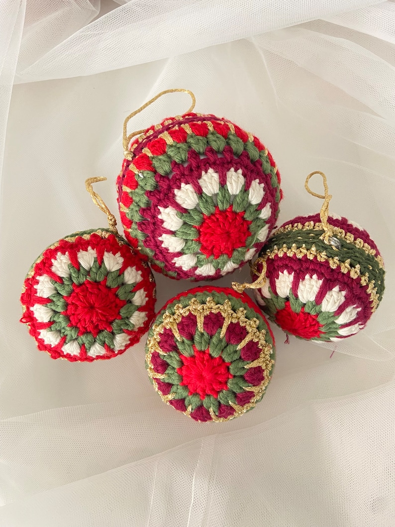 May include: Four crocheted Christmas ornaments in red, green, and white with gold accents. The ornaments are round and have a textured surface.