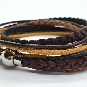 Op de afbeelding: Een meerstrengs leren armband met een gevlochten ontwerp. De armband is gemaakt van bruin en bruin leer en heeft een zilveren magneetsluiting.