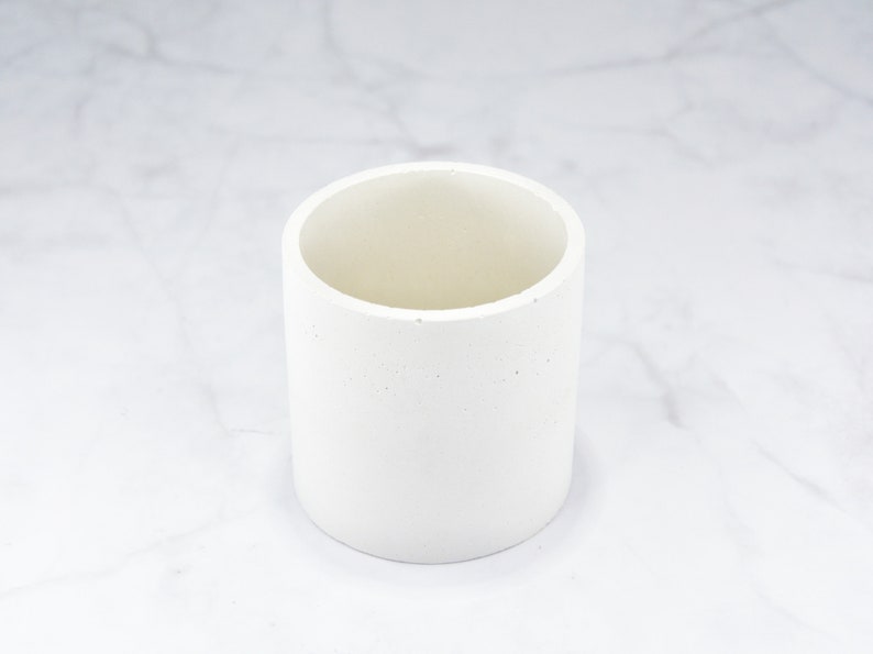 May include: A white cylindrical concrete planter with a rough texture.