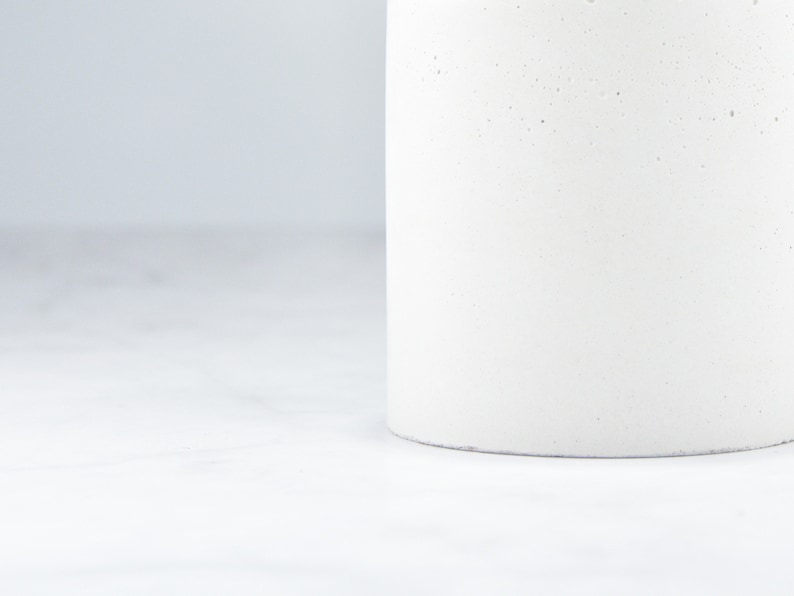May include: A white cylindrical concrete planter with a rough texture.