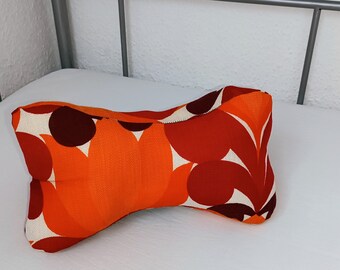 May include: A bright orange and red patterned neck pillow with a white background. The pillow is shaped like a bone and is made of fabric.
