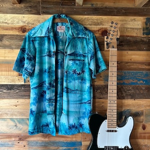 Könnte beinhalten: Ein blaues und weiß gemustertes Hawaiihemd mit Knopfleiste und kurzen Ärmeln. Das Hemd hängt an einem Holzbügel und hat ein Etikett mit der Aufschrift "Tailor Made".