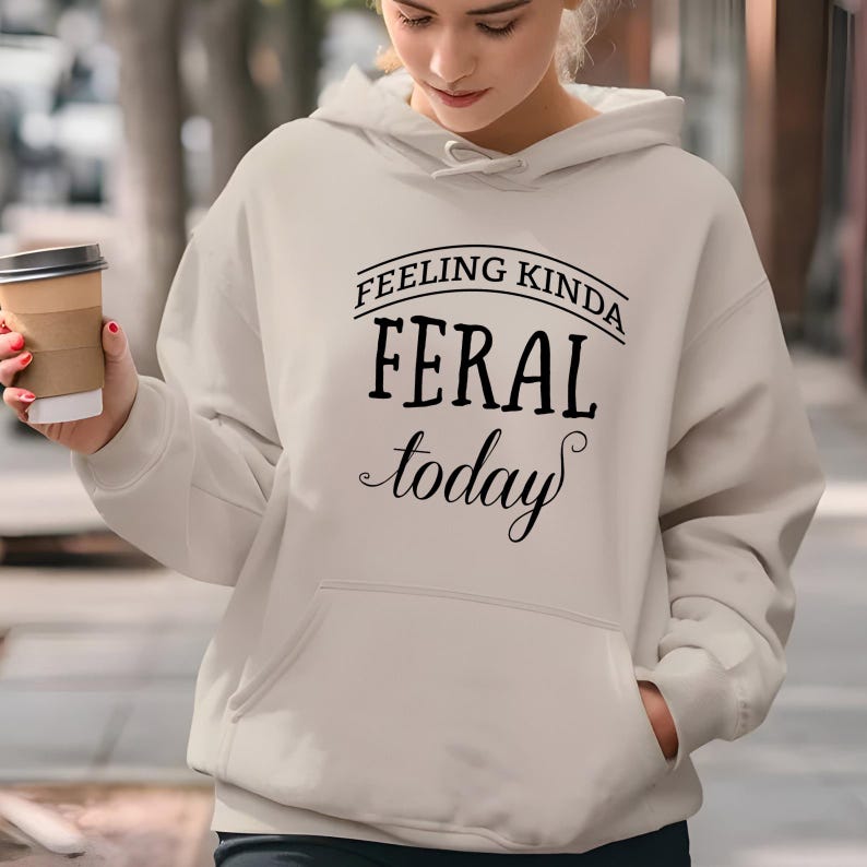 May include: A light beige hoodie with a black graphic that says "Feeling Kinda Feral Today".