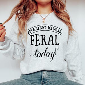May include: A gray sweatshirt with the text "Feeling Kinda Feral Today" printed in black.