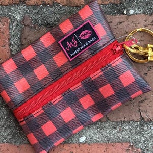 May include: Red and black buffalo plaid zippered pouch with a gold key ring attached. The pouch has a black label with the text "m&j makeup junkie bags".
