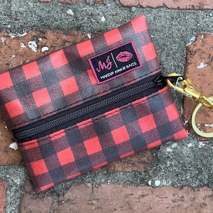 May include: A small red and black buffalo plaid zippered pouch with a gold key ring. The pouch has the text "MJ | Makeup Junkie Bags" printed on it.