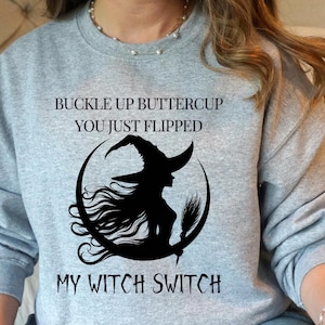 May include: Gray sweatshirt with a black witch silhouette riding a crescent moon and the text "Buckle up buttercup you just flipped my witch switch".