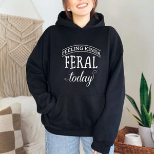 May include: Black hooded sweatshirt with the text "Feeling Kinda Feral Today" in white.