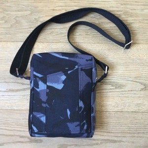 May include: A black and blue camouflage print crossbody bag with a black adjustable strap. The bag has a flap closure and a small pocket on the front.