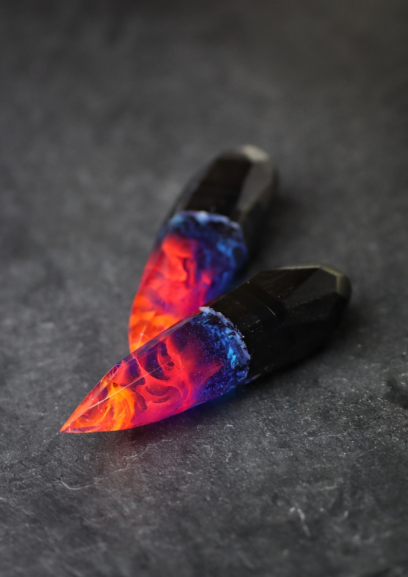 Puede incluir: Dos puntas de resina negra con un dise&ntilde;o rojo, naranja y azul en espiral. Las puntas tienen forma de cristal.