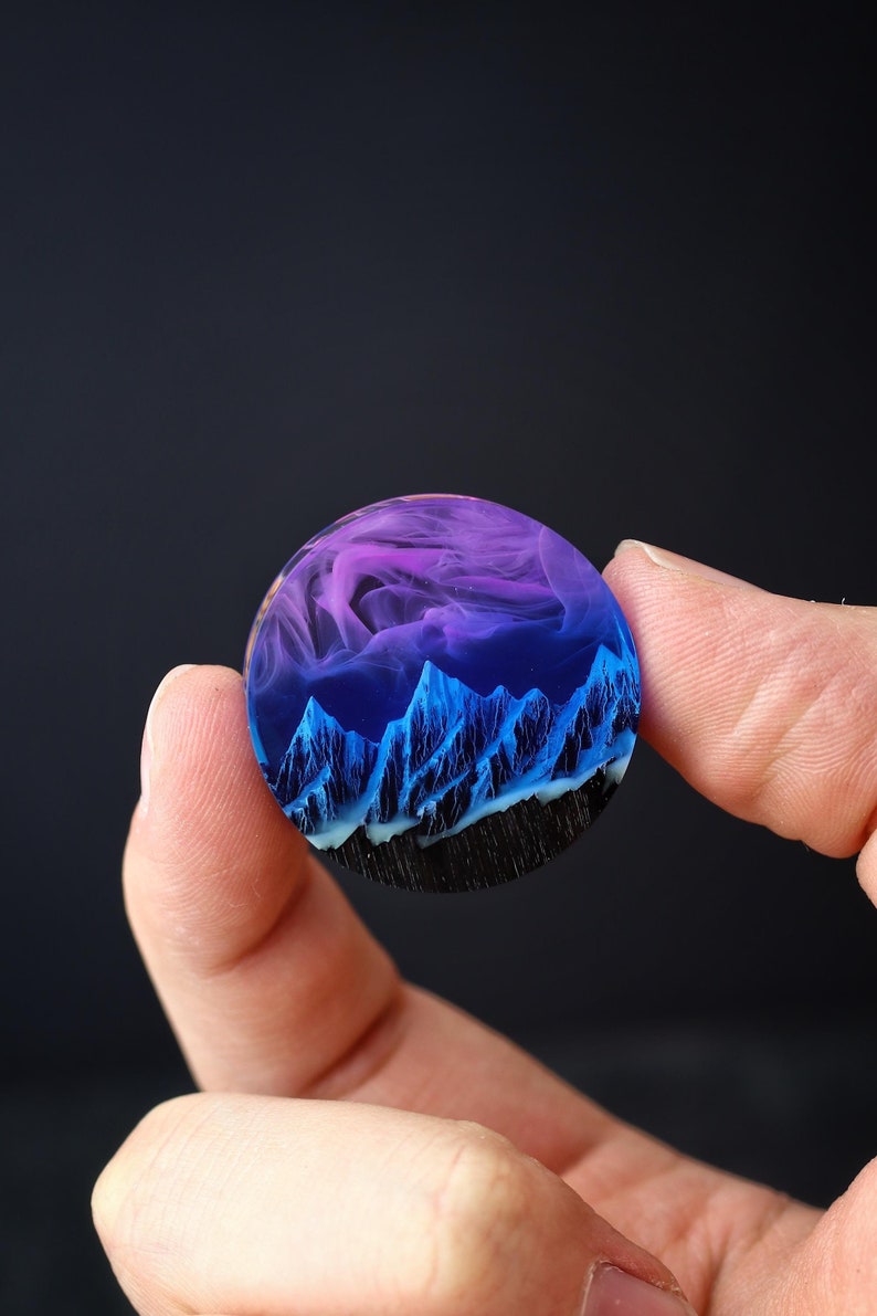 May include: A round resin pendant with a blue and purple mountain scene inside. The mountains are detailed and the resin is clear.