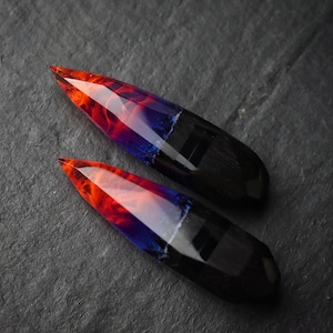 Puede incluir: Dos piezas largas y puntiagudas de resina con una base negra y un dise&ntilde;o rojo, naranja y azul en espiral.