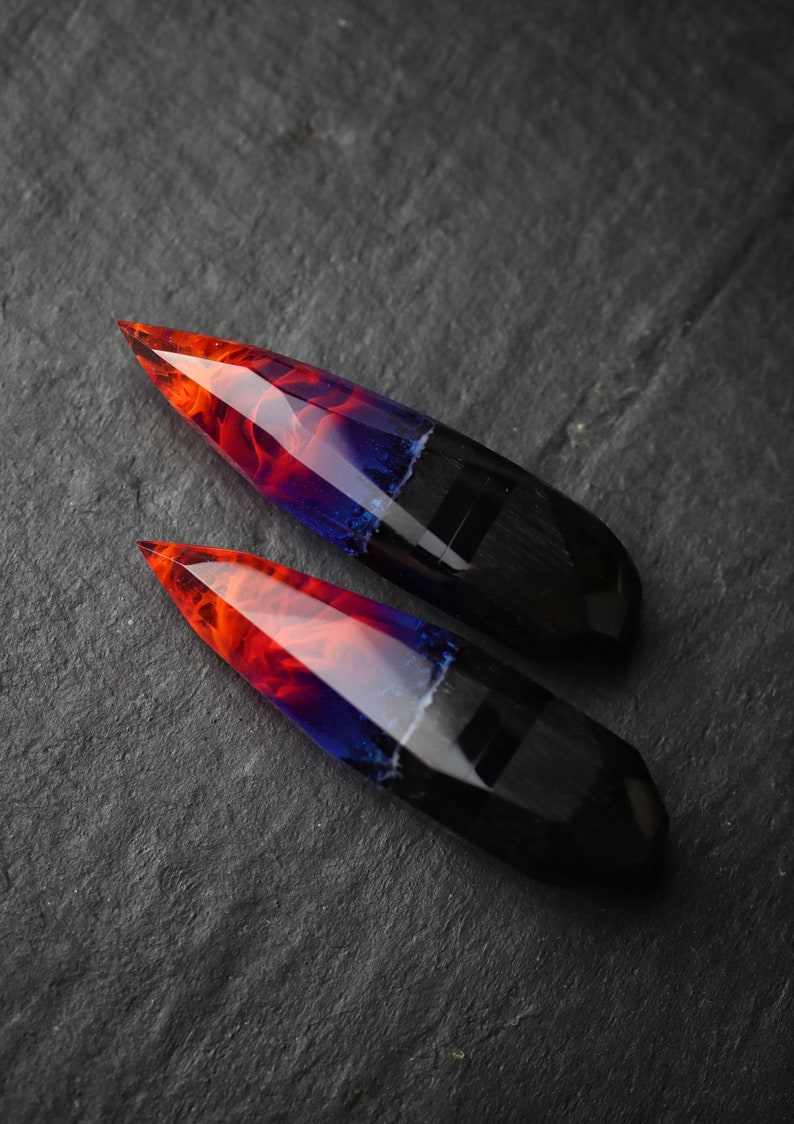 Puede incluir: Dos piezas largas y puntiagudas de resina con una base negra y un dise&ntilde;o rojo, naranja y azul en espiral.