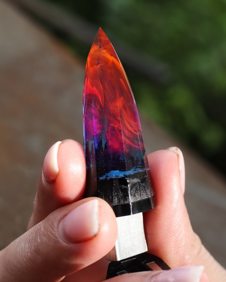 Puede incluir: Una unidad USB de resina puntiaguda y colorida con un patr&oacute;n de remolino de rojo, naranja, morado y azul. La unidad tiene forma de cristal o piedra preciosa.