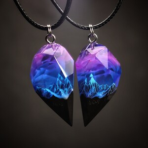 May include: Two matching pendant necklaces. Each pendant has a faceted, geometric shape with a black base and a translucent top. The top of each pendant has a gradient of purple and blue hues, with a mountain range design.