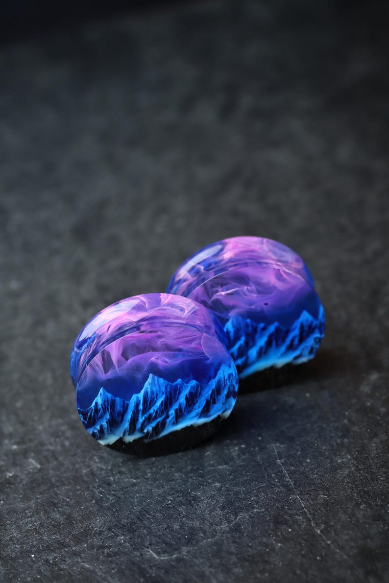 May include: A pair of purple and blue resin ear gauges with a mountain and sky design.