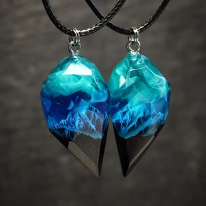 May include: Two matching pendant necklaces. Each pendant features a geometric shape with a black base and a clear resin top. The resin is filled with blue and white swirls and a mountain scene.