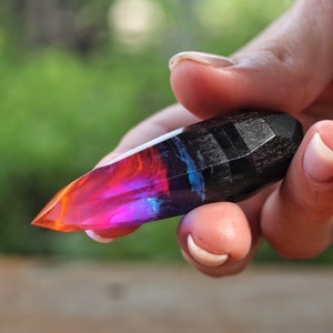 Puede incluir: Un cristal de resina puntiagudo multicolor con una base de madera negra. El cristal es una mezcla de rojo, naranja, rosa, azul y morado.