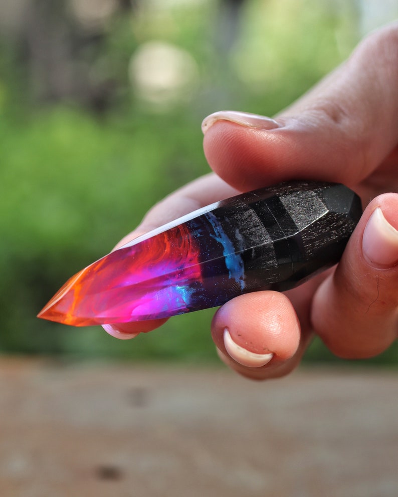 Puede incluir: Un cristal de resina puntiagudo multicolor con una base de madera negra. El cristal es una mezcla de rojo, naranja, rosa, azul y morado.