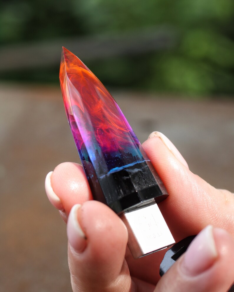 Puede incluir: Una unidad USB de resina colorida y multicapa con forma de punta de cristal. La unidad es negra en la base y tiene un conector USB plateado.